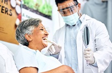 Patient smiling at reflection while dentist holds mirror