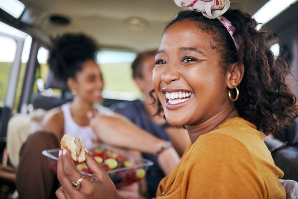 Woman in orange shirt smiling and eating a sandwich with her friends in a vehicle